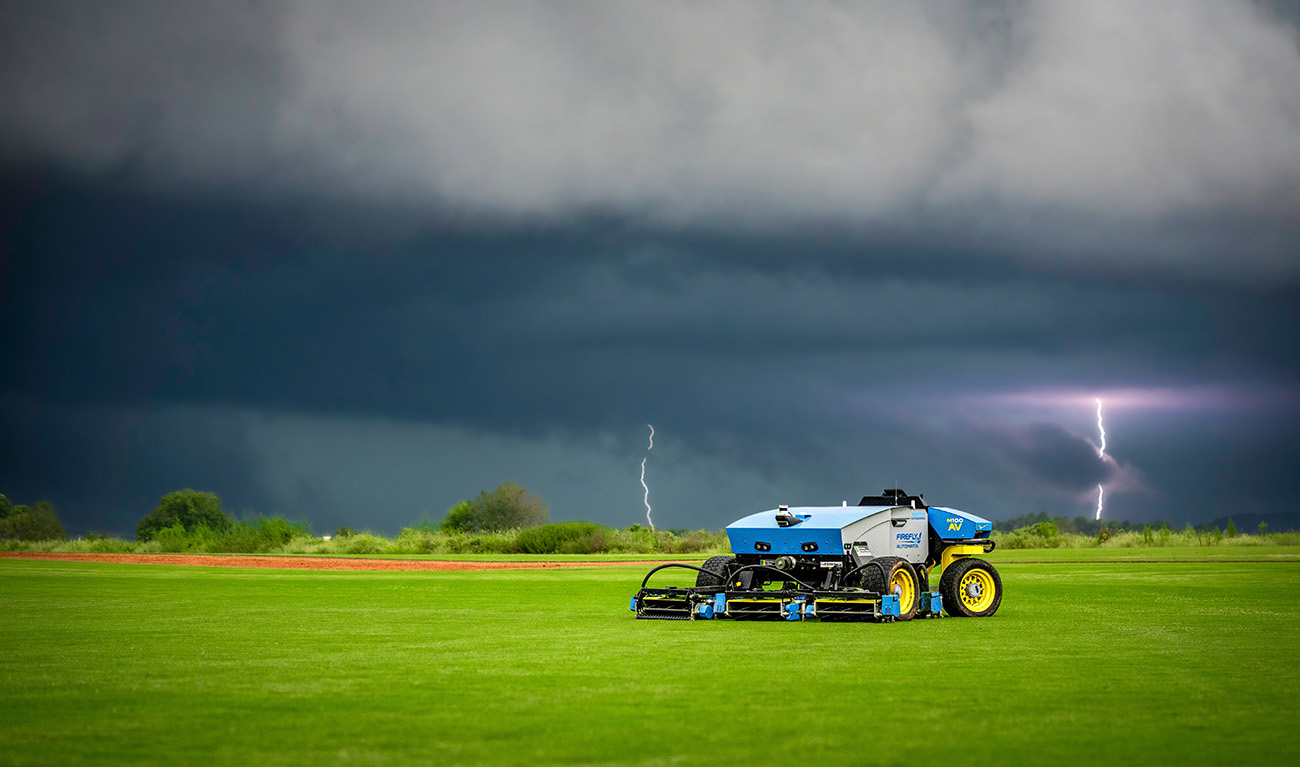 M100-AV mower in grassy field with lightning in sky