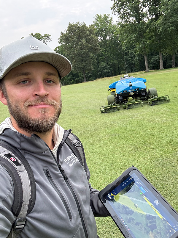 Jack Anderson holding tablet with FireFly AMP robotic mower in background on grass