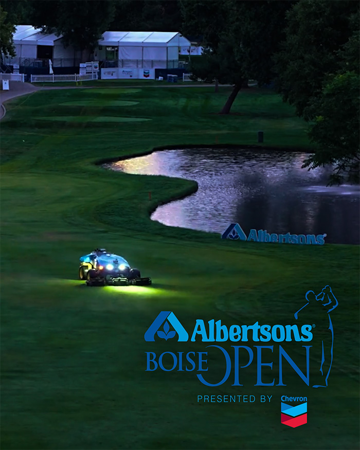 FireFly Automatix robotic fairway mower on dark golf course next to water hazard with Albertsons Boise Open tournament structures and logos